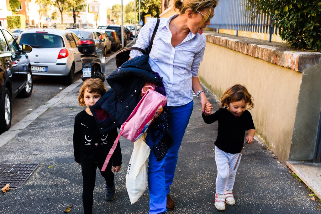 mom walking down the streets of Rome with her two girls showing tongue one girl eating mom's jacket