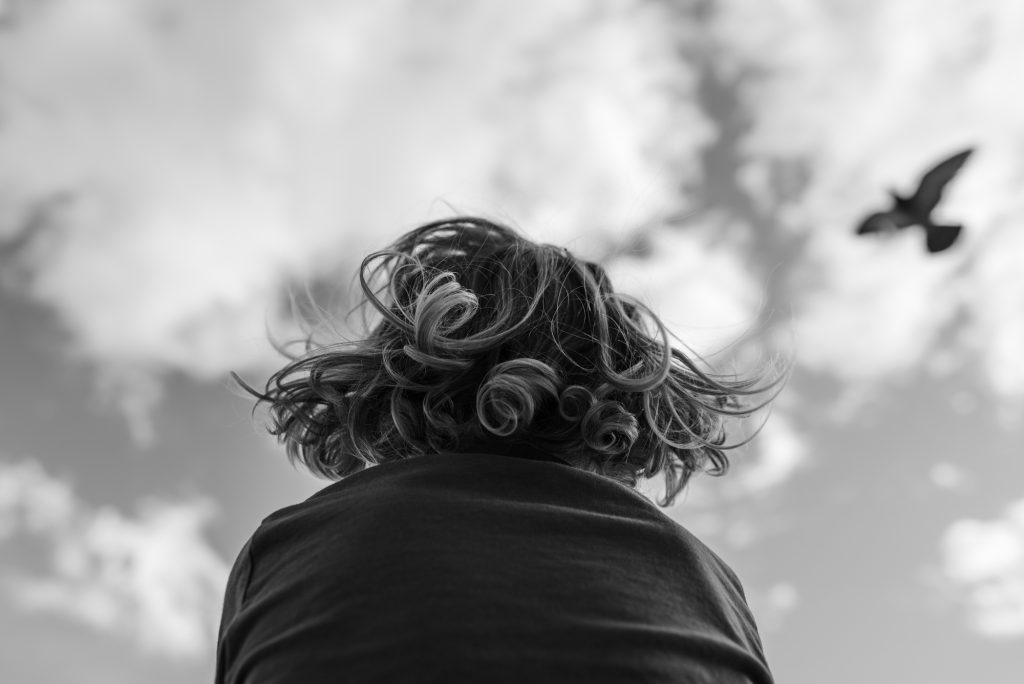 black and white photo, view from below, clouds, boy, curls, seagull flying, wide wings