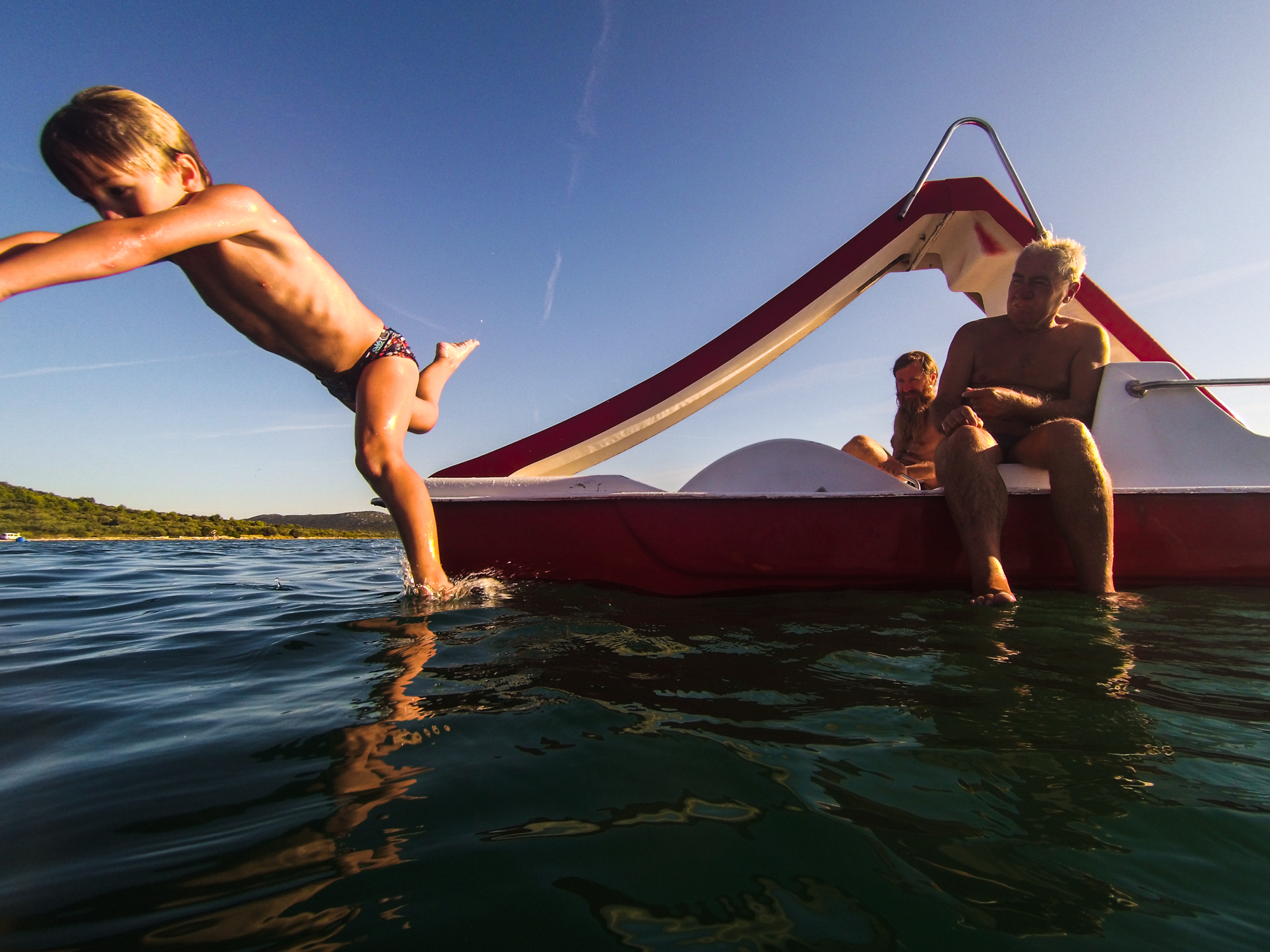 boy jumping into the sea from a red paddle boat croatia